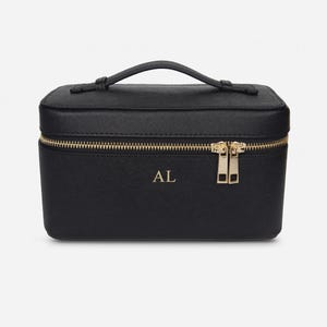 Può includere: Astuccio per il trucco rettangolare nero con cerniera e manico dorati. La custodia presenta le iniziali "AL" in lettere dorate. La cerniera e i dettagli del manico sono dorati.