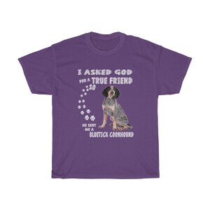 Pode incluir: Camiseta roxa com um gr&aacute;fico branco que diz "Eu pedi a Deus um verdadeiro amigo, ent&atilde;o ele me enviou um Bluetick Coonhound". O gr&aacute;fico tamb&eacute;m inclui um rastro de pegadas e um c&atilde;o Bluetick Coonhound.