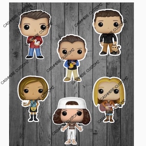 Könnte beinhalten: Sechs Popkultur-Vinylfiguren von Charakteren aus der Fernsehserie Friends. Die Figuren sind alle in verschiedenen Posen und tragen ihre charakteristischen Outfits. Die Figuren befinden sich auf einem Holzmaserungshintergrund.