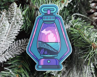 May include: A teal blue lantern sticker with a pink and purple sunset scene inside. The scene features the outline of Michigan's Upper Peninsula and the word "Michigan" in a black script font.