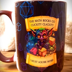 May include: A brown ceramic mug with a colorful illustration of a goblin surrounded by dice and the text "The math rocks go clickity clackity I must acquire more!"