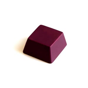 May include: A solid, plum-colored, rectangular object with a beveled edge. The object is a deep shade of purple and sits on a white background. The shape is a truncated pyramid, with a flat top and angled sides.