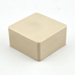 May include: A beige square block with softly rounded corners. The object has a smooth, matte surface and appears to be made from a single material. The cube is set against a white backdrop.
