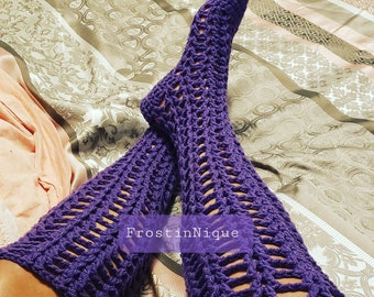 May include: Purple crochet leg warmers with a lacy design. The leg warmers are worn on a person's legs. The text "FrostinNique" is visible on the leg warmers.