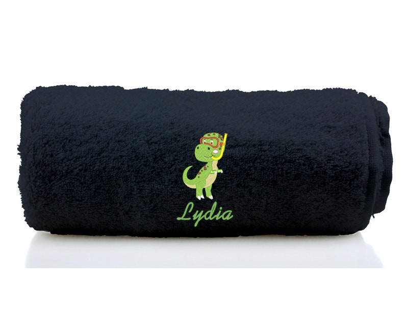 K&ouml;nnte beinhalten: Schwarzes Badetuch mit einem gr&uuml;nen Dinosaurier, der einen Schnorchel und eine Taucherbrille tr&auml;gt. Das Handtuch ist mit dem Namen "Lydia" bestickt.