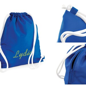 Puede incluir: Una bolsa de cord&oacute;n azul con cordones blancos y un bolsillo con cremallera. La bolsa tiene el nombre "Lydia" bordado en verde en la parte delantera.