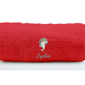 K&ouml;nnte beinhalten: Rotes Badetuch mit einem Cartoon-Hai, der einen Schnorchel und eine Taucherbrille tr&auml;gt. Das Handtuch ist aufgerollt und der Name "Lydia" ist auf das Handtuch gestickt.
