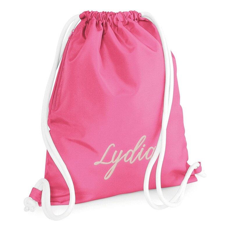 Puede incluir: Bolsa de deporte rosa con cordones blancos y el nombre "Lydia" bordado en color crema.