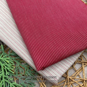 May include: Two folded pieces of fabric featuring a pinstripe pattern. One piece is deep red with thin white vertical stripes, while the other is off-white with thin red vertical stripes. The fabric has a visible woven texture throughout.