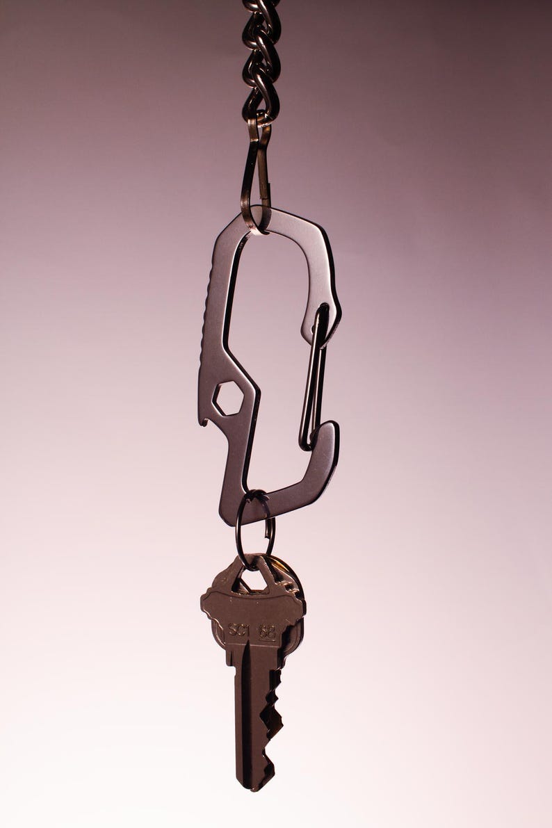 Op de afbeelding: Een zilveren karabijnhaak met een flesopener bevestigd aan een ketting. Een sleutelbos is bevestigd aan de karabijnhaak.