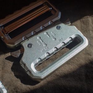 May include: A silver metal belt buckle with a sliding buckle mechanism. The buckle has the text "Made in USA" and "8621" engraved on it.