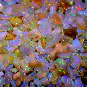 May include: A close-up view of a collection of iridescent opal gemstones. The opals are various shapes and sizes, with a rainbow of colors shimmering on their surfaces.