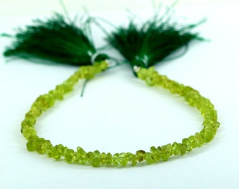 May include: A delicate necklace featuring small, irregular, light green peridot gemstones. The necklace is accented with dark green tassels at each end. The gemstones are strung together, creating a subtle, natural look.