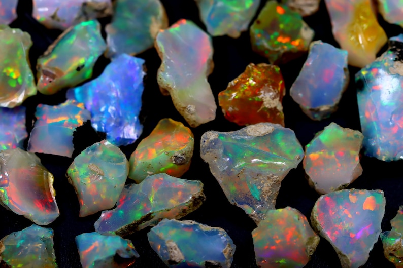 May include: A collection of rough opal gemstones in various shades of blue, green, red, and orange. The opals are iridescent and have a natural, unpolished finish.