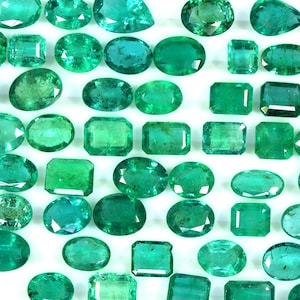 May include: A collection of emerald green gemstones of various shapes and sizes, including oval, rectangular, and square cuts. The gemstones are arranged on a white background.