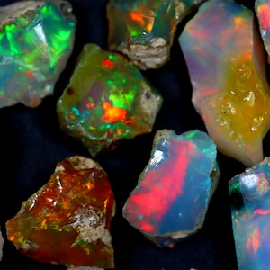 May include: A collection of rough opal gemstones in various shades of green, red, and yellow. The opals are iridescent and have a natural, raw appearance.