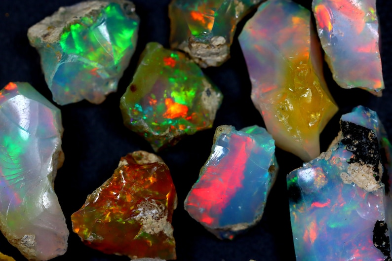 May include: A collection of rough opal gemstones in various shades of green, red, and yellow. The opals are iridescent and have a natural, raw appearance.
