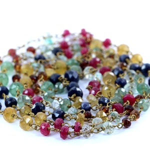 Puede incluir: Un collar de piedras preciosas multicolores con una cadena de oro. El collar presenta cuentas facetadas en tonos de azul, verde, amarillo y rojo.
