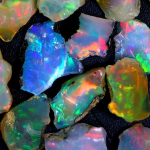 May include: A collection of rough opal gemstones in various shades of blue, green, red, and orange. The opals are iridescent and have a natural, unpolished finish.
