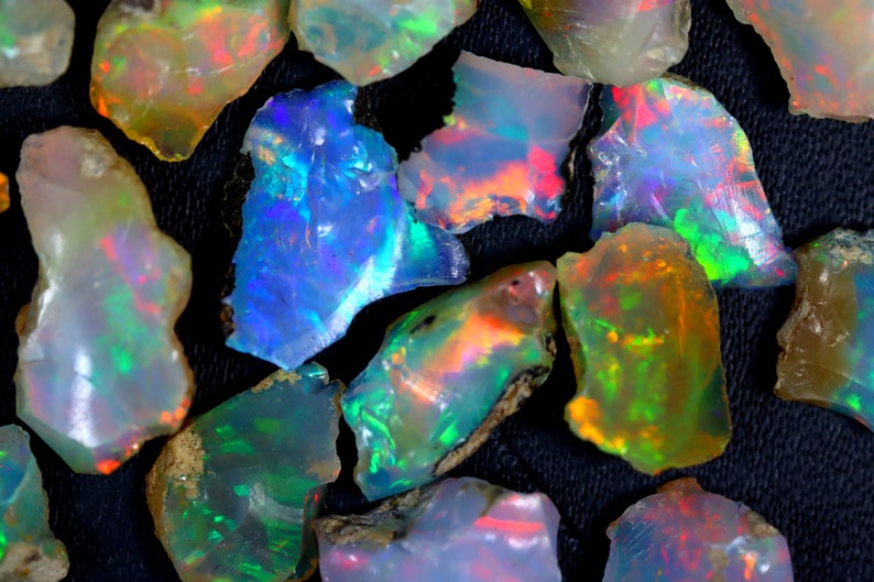 May include: A collection of rough opal gemstones in various shades of blue, green, red, and orange. The opals are iridescent and have a natural, unpolished finish.