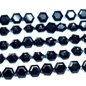 May include: A collection of black faceted gemstone beads, arranged in rows on a white background. The beads are hexagonal in shape and have a polished finish.