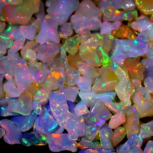 May include: A collection of iridescent opal gemstones in various shapes and sizes. The opals are a mix of white, pink, and blue with flashes of green and orange.