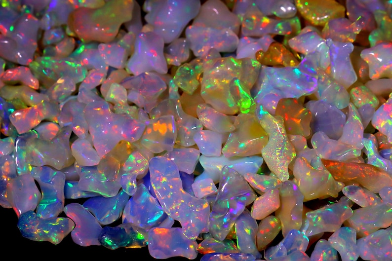 May include: A collection of iridescent opal gemstones in various shapes and sizes. The opals are a mix of white, pink, and blue with flashes of green and orange.
