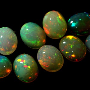 May include: A collection of nine oval-shaped opals with iridescent colors, including green, blue, red, and yellow.