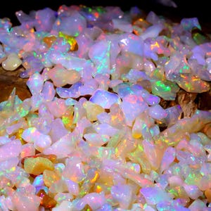 May include: A large pile of iridescent opal gemstones in various shapes and sizes. The opals are a mix of white, pink, and yellow with flashes of green and blue.