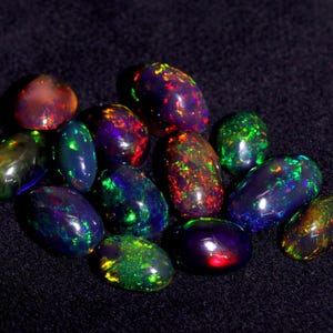Pode incluir: Uma cole&ccedil;&atilde;o de opalas pretas de forma oval com cores iridescentes, incluindo verde, vermelho, azul e roxo.