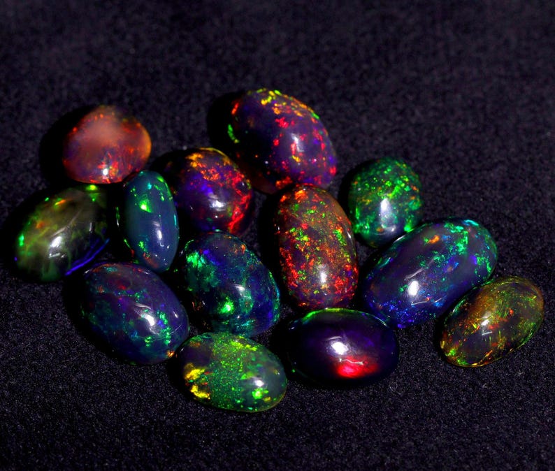 Pode incluir: Uma cole&ccedil;&atilde;o de opalas pretas de forma oval com cores iridescentes, incluindo verde, vermelho, azul e roxo.