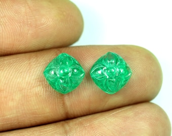 May include: Two green emerald gemstones carved with a floral design. The gemstones are square shaped and have a polished finish.