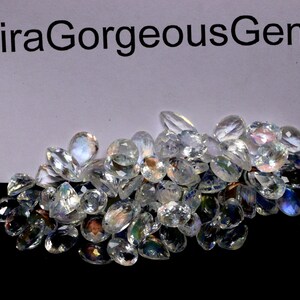 May include: A pile of clear, faceted gemstones with iridescent flashes of color. The gems are various shapes, including teardrops and ovals. The text "AqiraGorgeousGems" is at the top.
