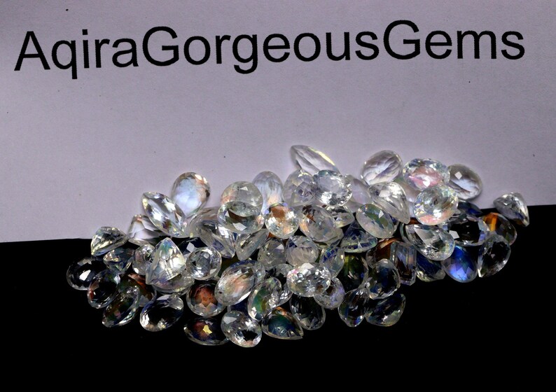 May include: A pile of clear, faceted gemstones with iridescent flashes of color. The gems are various shapes, including teardrops and ovals. The text "AqiraGorgeousGems" is at the top.