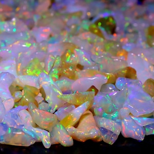 May include: A large pile of iridescent opal gemstones in various shapes and sizes. The opals are a mix of white, yellow, and green.