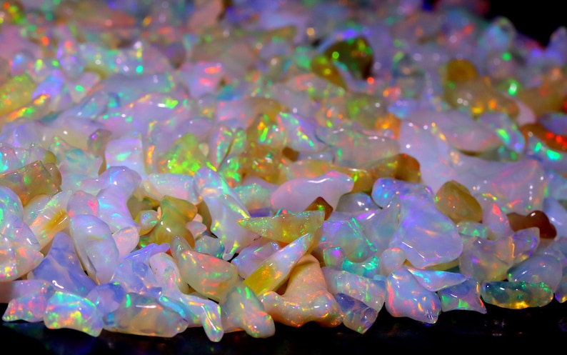May include: A large pile of iridescent opal gemstones in various shapes and sizes. The opals are a mix of white, yellow, and green.
