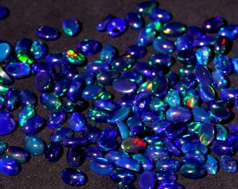 Pode incluir: Uma coleção de pedras preciosas de opala azul, verde e iridescente. As pedras de forma ovalada estão dispostas em um padrão aleatório sobre um fundo preto.