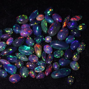 May include: A collection of iridescent opal gemstones in various shades of purple, blue, and green. The gemstones are oval-shaped and have a smooth, polished finish.