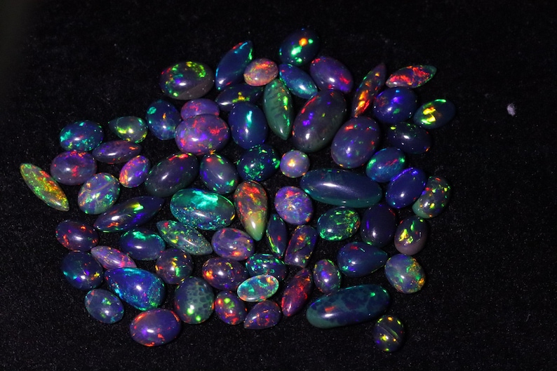 May include: A collection of iridescent opal gemstones in various shades of purple, blue, and green. The gemstones are oval-shaped and have a smooth, polished finish.