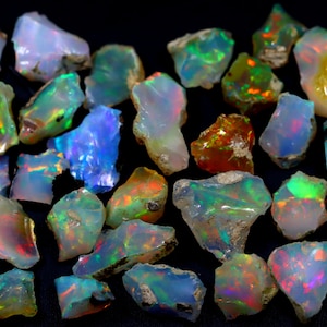May include: A collection of rough opal gemstones in various shades of green, blue, red, and orange. The opals are iridescent and have a natural, unpolished finish.