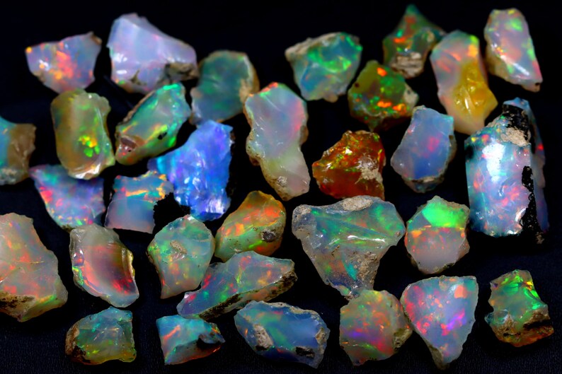 May include: A collection of rough opal gemstones in various shades of green, blue, red, and orange. The opals are iridescent and have a natural, unpolished finish.