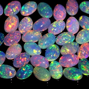 Puede incluir: Una colección de ópalos de forma ovalada con colores iridiscentes, incluyendo rosa, azul, verde y amarillo. Los ópalos están dispuestos en un patrón aleatorio sobre un fondo negro.