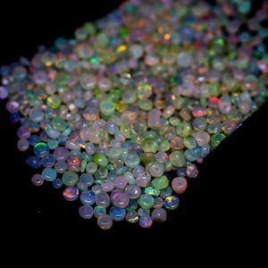 May include: A collection of small, iridescent opal gemstones. The opals display a variety of colors, including blue, green, red, and yellow, with a milky white base. The gemstones are scattered against a black background.