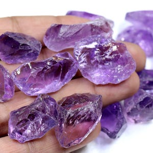 May include: A collection of raw amethyst crystals in various sizes and shapes. The crystals are a deep purple color and have a natural, rough texture.