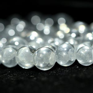 Peut inclure: Gros plan sur des perles sphériques transparentes. Les perles sont claires et réfléchissent la lumière, créant un effet scintillant. Le fond sombre fait ressortir les perles. Les perles font probablement partie d'un collier ou d'un bracelet.