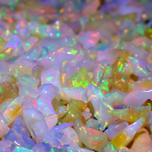 Może przedstawiać: Widok z bliska na stos opalowych kamieni szlachetnych o tęczowych barwach. Opale mają różne odcienie bieli, różu i zieleni, z migocącym, tęczowym efektem.