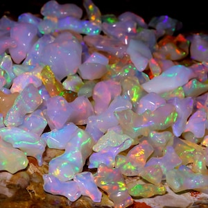 May include: A collection of iridescent opal gemstones in various shapes and sizes. The opals are a mix of white, pink, and green with a rainbow sheen.