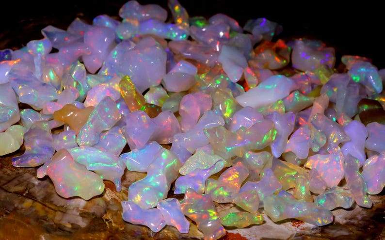 May include: A collection of iridescent opal gemstones in various shapes and sizes. The opals are a mix of white, pink, and green with a rainbow sheen.