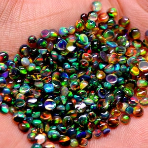 May include: A large pile of iridescent opal gemstones in various shades of green, blue, red, and gold. The gemstones are round and have a smooth, polished finish.