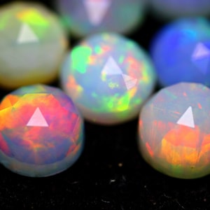 May include: Close-up of several faceted opal gemstones. The opals display a range of colors, including red, orange, green, and blue, with a white triangular facet at the top of each stone. The gemstones are set against a black background.
